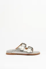 Sandalias de cuero color negro con dos tiras anchas sobre el empeine, cada una con hebillas metálicas ajustables y detalles de tachas plateadas. La suela es de cuero con un borde de color madera.