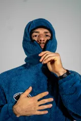 Canguro de textura tipo peluche en color azul, con cierre frontal parcial, cuello alto y bolsillo tipo canguro. Presenta un parche ovalado en el pecho con diseño gráfico.