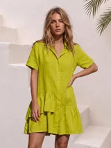 Vestido camisero verde lima de lino, con mangas cortas, cierre frontal abotonado y detalle de volados asimétricos en el ruedo.