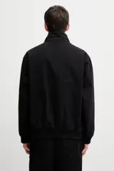Campera Carhartt WIP modelo Ravon Jacket, de color negro, con cuello alto, cierre frontal completo con cremallera y bolsillos frontales. Cuenta con el parche con el logotipo de la marca en el bolsillo izquierdo y puños y dobladillo elásticos.