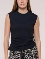 Blusa blanca de corte entallado y textura acanalada, con escote redondo a la base y diseño sin mangas. Presenta un detalle de drapeado lateral sujetado por una hebilla metálica circular en la cintura.