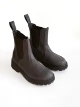 Bota tipo Chelsea de caña media, confeccionada en cuero negro con acabado mate. Presenta paneles elásticos laterales, tiradores traseros y suela track robusta con plataforma dentada.