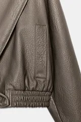 Cazadora Zara Woman Collection de efecto piel con cuello solapa ancho, manga larga, bolsillos delanteros y bajo elástico. Presenta un cierre frontal cruzado con botón a presión.