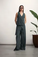 Pantalón de corte amplio y tiro alto, confeccionado en tela con textura tipo lino. Presenta un diseño envolvente en la cintura con un lazo lateral para anudar, creando un efecto de superposición frontal.