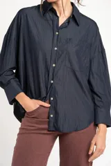 Camisa azul marino de corte oversize, con cuello clásico, cierre frontal con botones, mangas largas con puños anchos y un bolsillo aplicado en el pecho.