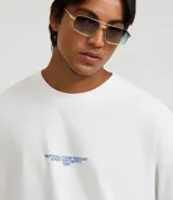 Remera oversized de algodón color blanco, con cuello redondo, manga corta y una estampa trasera en azul de estilo renacentista con la frase "Running from destiny singe antiquity".