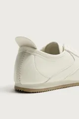 Zapatilla de estilo retro con cordones, confeccionada en una combinación de piezas de cuero sintético en color blanco, con suela dentada de goma en tono caramelo.