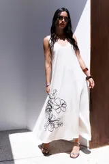 Vestido largo de corte holgado en color azul, con escote en V, breteles regulables y bolsillos laterales. Presenta un delicado diseño de flores bordadas en el lateral inferior.