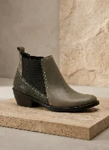 Bota tipo Chelsea de cuero negro con paneles laterales elásticos y taco bajo cuadrado. Presenta una combinación de texturas en el cuero y una presilla trasera para facilitar el calce.