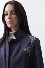 Blazer de gamuza color terracota con bordados decorativos en color crudo en solapas, puños y ruedo. Presenta corte recto, solapas clásicas y cierre frontal con un botón forrado.