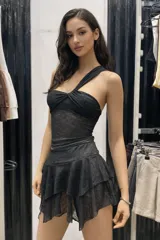 Conjunto de dos piezas compuesto por un top asimétrico de un solo hombro con detalle fruncido en el busto y una pollera corta con volados, ambos confeccionados en tejido de encaje negro semitransparente.