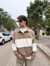 Buzo tipo polo de corte relajado y fit boxy, con diseño de bloques de color en tonos marrón y blanco. Presenta cuello polo con cierre de botones y bordado pequeño en el pecho.