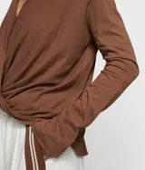 Blusa cruzada de punto de algodón orgánico color marrón, con cuello, cierre de botón, puños con abertura y monograma bordado en la manga izquierda. Tiene bajo recto y aberturas laterales.