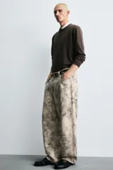 Pantalón de corte relajado confeccionado en algodón, con diseño de efecto lavado y estampado abstracto en tonos grises y beige. Presenta cinco bolsillos y cierre frontal con cremallera y botón.