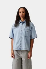 Camisa de denim de algodón celeste, de corte holgado y mangas cortas, con cierre frontal de botones metálicos y un bolsillo aplicado en el pecho con etiqueta de la marca.