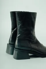 Bota de caña media confeccionada en cuero negro, con diseño minimalista, punta cuadrada y taco ancho geométrico.
