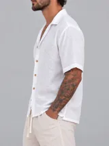 Camisa de manga corta color blanco, de corte holgado, con cuello tipo solapa y cierre frontal de botones.