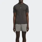 Remera deportiva gris oscuro de manga corta, con logo reflectante de Reebok en el pecho y paneles de malla en hombros y laterales.