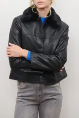 Chaqueta corta color beige con cuello de piel sintética negra, cierre frontal de botones y bolsillos laterales.