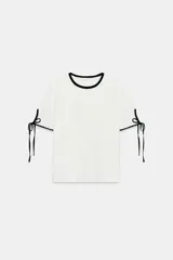Camiseta de algodón de corte regular, color blanco con detalles de vivos y lazos en contraste negro en el cuello y en las mangas cortas.