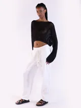 Sweater crop negro de punto abierto y manga larga con brillo sutil. Presenta escote bote y diseño relajado.
