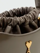 Minibolso tipo bucket de piel lacada color gris, con cierre de cordón ajustable y detalle de logo metálico dorado en forma de corazón con letra A. Cuenta con asa superior fija.