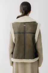 Chaleco de piel sintética en color chocolate, con cierre frontal y detalles de cuero en los bordes. Presenta un diseño de cuello solapa y ajuste lateral con hebillas.