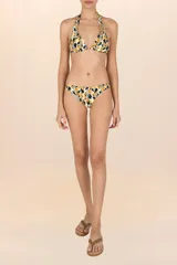 Top de bikini con estampado abstracto en tonos amarillo mostaza, negro y blanco. Diseño de cuello halter con tiras ajustables y detalle metálico dorado con forma de hoja en la unión de las copas.