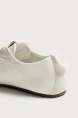 Zapatillas de cuero color blanco roto, de diseño minimalista con cordones, suela fina de goma marrón y detalles de gamuza en la puntera y los ojales.