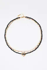 Collar de diseño multicapa compuesto por una tira de cuentas de cristal negro con un dije central en forma de corazón dorado, una fina cadena dorada con pedrería y otra cadena dorada decorada con pequeñas cuentas de colores.