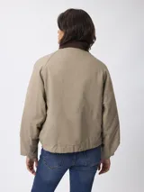 Campera corta de algodón en color beige, con cuello camisero en contraste color marrón, cierre frontal con botones a presión y dos bolsillos frontales tipo cargo.