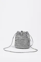 Bolso mini tipo saco confeccionado con tiras entrelazadas color plateado, con cierre de cordón ajustable y correa larga trenzada.