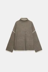 Jersey de punto con cuello subido y manga larga, de corte holgado. Presenta detalles de vivos en color crema en el cuello, puños y costuras de las mangas, contrastando con el tono marrón jaspeado de la prenda.