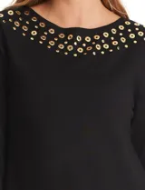 Buzo de punto negro con cuello redondo, manga larga y detalle de tachas metálicas doradas en el escote y a lo largo de la manga derecha.