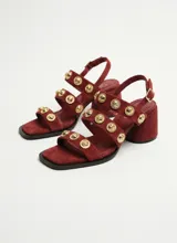 Sandalias de gamuza color bordó, con múltiples tiras delanteras decoradas con botones dorados metálicos, taco cuadrado y tira ajustable al tobillo con hebilla.