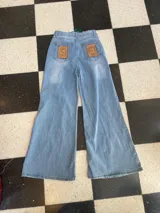 Jeans de mezclilla celeste de corte wide leg, con parches de cuero genuino bordados a mano en los bolsillos traseros.