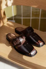 Sandalias tipo mule de cuero marrón con puntera cuadrada, diseño abierto y hebilla ajustable.
