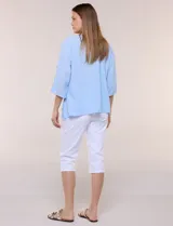 Blusa Erika de algodón con estampado de rayas en tonos azules, rosados y amarillos. Presenta cuello redondo con escote en V y botones frontales, mangas cortas decoradas con una fila de botones en los laterales y dobladillo asimétrico.