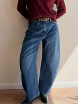 Pantalón de jean con corte balloon fit, de tiro alto y diseño holgado en las piernas. Confeccionado en denim con elastano, presenta un lavado azul clásico y cierre frontal con botón y cremallera.