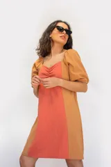 Vestido corto de algodón en calidad tusor con diseño en bloque de color, combinando un panel central coral con laterales y mangas abullonadas en color tostado. Presenta escote cuadrado con frunce en el centro del busto.