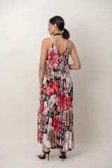 Vestido largo de seda plisada con estampado floral en tonos rojos, rosados y blancos sobre base oscura, con tirantes finos y escote en V.