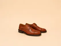 Zapato de vestir tipo oxford en cuero color marrón, con detalle de picado en la puntera y cordones al tono.