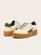 Zapatillas Sorel modelo Ona Ave T-Toe con diseño retro y plataforma. Presentan una combinación de cuero y gamuza en tonos crema, con detalles en verde oliva y suela de caucho color caramelo con textura estriada.