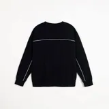 Buzo negro de corte holgado con cuello redondo, confeccionado en frisa invisible premium. Presenta detalles de vivos en color blanco en los laterales y en la espalda, y cuenta con una etiqueta decorativa en el frente.