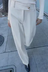 Pantalón blanco de tiro alto con pernera recta y pinzas marcadas en el frente. Cierre frontal con botón metálico dorado.