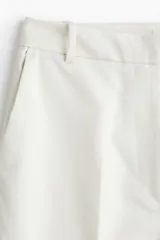 Pantalón sastrero color blanco, de tiro alto y corte recto, con pinzas y bolsillos laterales.