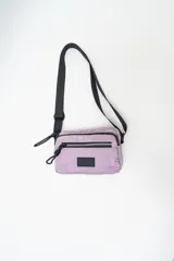Cartera tipo bandolera de nylon color lila, con cierre frontal y correa ajustable negra.