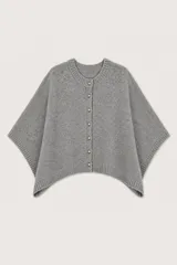Poncho de punto color gris, con diseño de corte asimétrico, cuello redondo y cierre frontal con botones metálicos. Presenta terminaciones en tejido acanalado en el cuello, los bordes laterales y el ruedo.