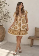Vestido corto beige de corte oversized, con escote en V, mangas cortas y estampado geométrico en tonos mostaza.