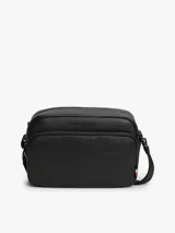 Bandolera Tommy Hilfiger de color negro, confeccionada en poliuretano con diseño de compartimento principal con cierre de cremallera y bolsillo exterior frontal con panel de textura tejida. Cuenta con correa ajustable, bolsillo interior con cierre y detalles distintivos de la marca con logo metálico en la parte delantera.